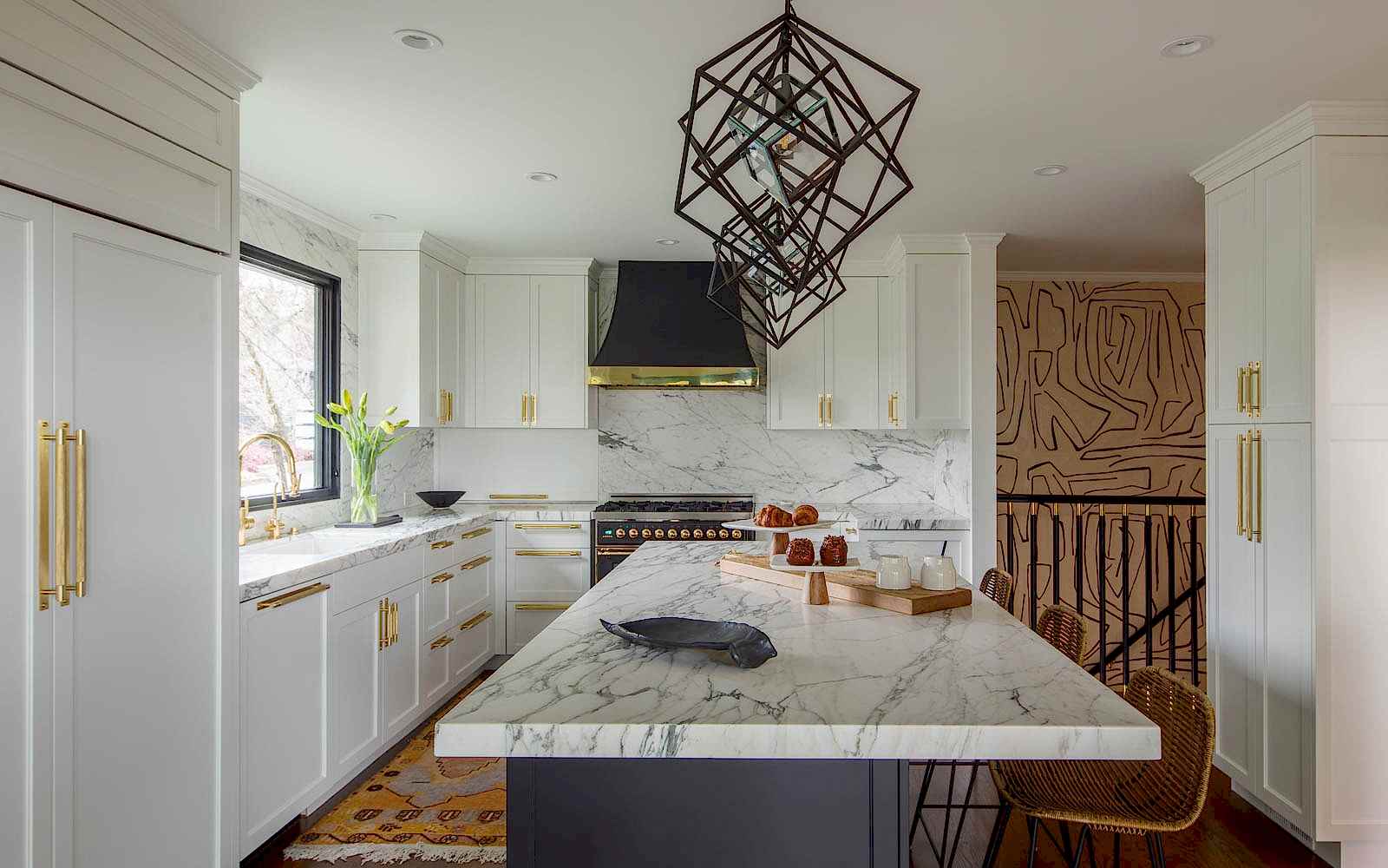 Side view of a kitchen with marble countertops, pendant lights, and an accent wall by the back stairwell. 