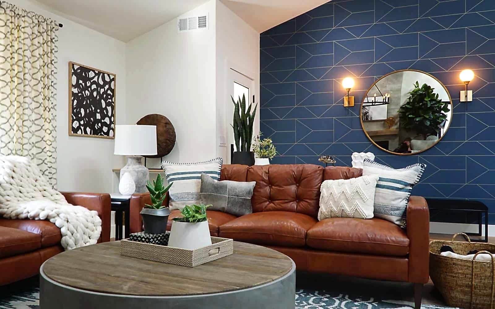 A modern ranch style home's living room. Two leather sofas surround a round coffee table, with a blue accent wall in the background. 